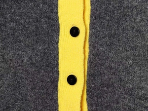 Detail of color-block knitwear with grey wool fabric and yellow trim with black buttons