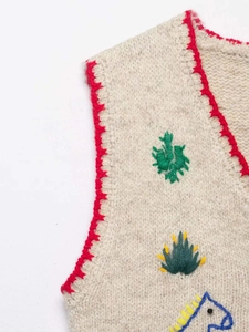 Detail of oat-colored knit vest with red scalloped trim and botanical cactus embroidery