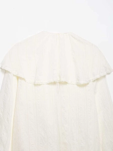 Détail d'une chemise blanc cassé avec un grand col châle et des bordures en dentelle délicate
