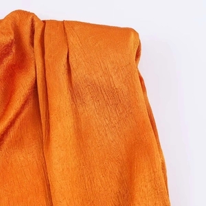 Detail of the stand collar and pleated shoulder design on a bright orange sleeveless vest