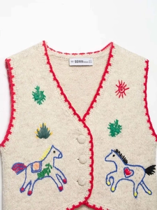 Detailed close-up of V-neck knit vest featuring red scalloped edges and colorful embroidery