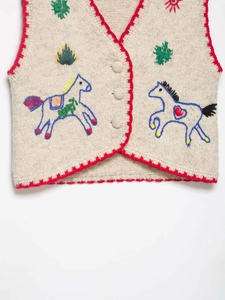 Detail of knit vest featuring red scalloped edges and colorful horse embroidery motifs