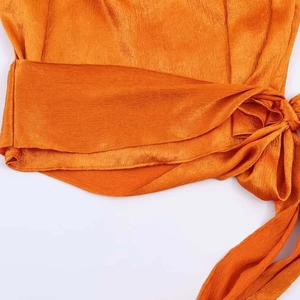 Detailed view of bright orange textured fabric with side bow tie-up knot and soft pleats