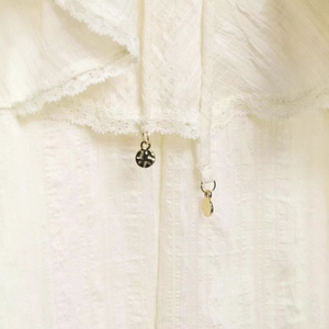 Chemisier blanc élégant avec textures verticales, bordures en dentelle et pendentifs en métal