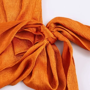 Detail of bright orange sleeveless top showing pleated texture and bow tie detail