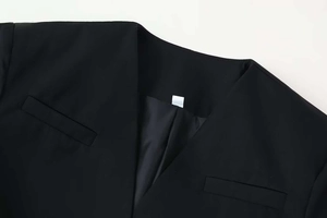 Detail of minimalist black V-neck blazer collar showing refined texture and clean pocket seams