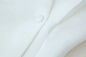 Close-up detail of white blazer featuring premium fabric texture and matching cloth button