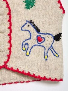 Detail of knit vest featuring red scalloped edges and horse embroidery with sequins