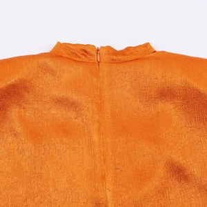 Detail of high collar and textured fabric on vibrant orange sleeveless top with zipper