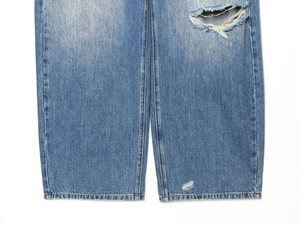 Detail view of light blue distressed denim jeans with ripped holes and whiskers texture