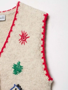 Detail of beige knit vest featuring red scalloped edges and colorful sun embroidery