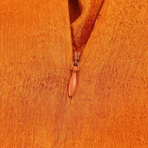 Detail of an orange sleeveless top showing the invisible zipper and pleated fabric texture