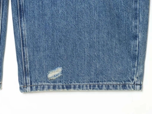 Close-up of distressed denim fabric with vintage wash and frayed hole detail