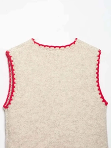 Close-up of oatmeal knitted vest with red scalloped crochet trim on neckline and armholes