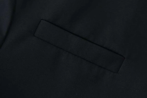 Close-up of a classic flap pocket on a tailored black blazer with textured fabric