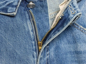 Detailed close-up of YKK metal zipper and denim button on retro high-waist jeans