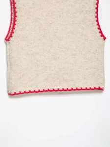 Detail of cream knit vest featuring red crochet trim on the hem and textured fabric
