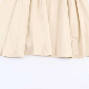 Detailed macro view showing the pleated hem and precise stitching of the beige dress
