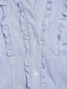 Detailed view of blue and white striped shirt featuring ruffled trim and clear buttons