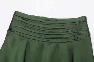 Detail of dark green satin mini skirt showing layered pleats and silky fabric texture