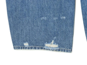 Macro shot of vintage mid-blue denim jeans featuring distressed hem and ripped details
