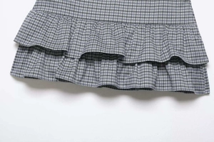 Detailed close-up showing the double-layered ruffle hem of a plaid skirt in blue and grey