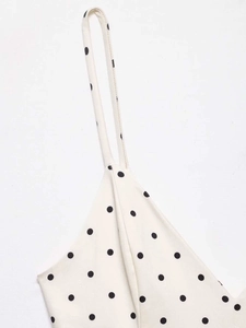Detailed close-up of white polka dot fabric with black dots and thin shoulder strap