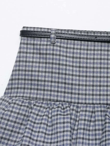 Detail of blue plaid skirt waist featuring pleats and a slim black leather belt