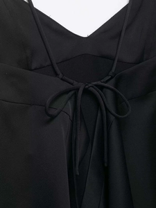 Detail of minimalist black V-neck top showing thin straps and cross-tie back knot