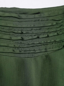 Detail view of dark green satin mini skirt showing layered pleats and textured fabric