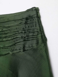 Detail of dark green satin mini skirt showing side invisible zipper and layered pleats