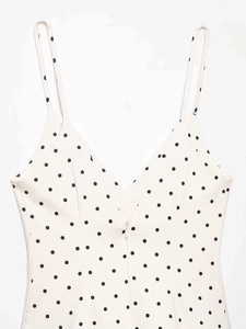 Close-up of a white polka dot top featuring a V-neck, thin straps and a front zipper detail