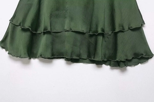 Detail view of double-layered ruffle hem on a dark green satin textured mini skirt