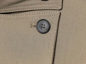 Close-up of matte black buttons and precision stitching on khaki double-breasted coat
