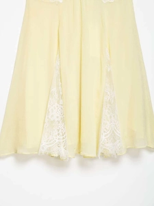 Close-up of light yellow chiffon hem with intricate white lace panels and floral details