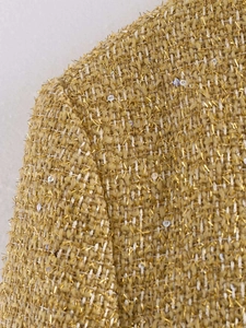 Detailed macro shot of yellow tweed fabric with interwoven gold thread and clear sequins