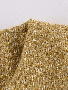 Detailed macro view of golden tweed fabric with metallic yarn and sequin embroidery