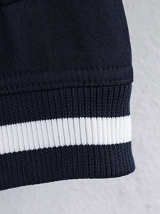 Detail of navy blue twill fabric jacket featuring white striped ribbed cuffs and hem