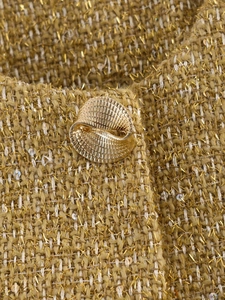 Detailed macro view of yellow tweed fabric with metallic gold thread and a spiral button