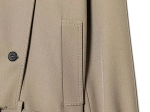 Macro detail of khaki trench coat featuring a black button and reinforced flap pocket seams