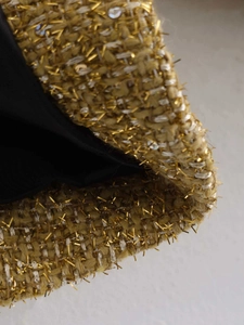 Detail of gold tweed fabric with metallic threads and sequins featuring a black lining