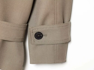 Macro detail of khaki trench coat cuff with black button and fine stitching details