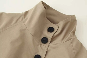 Detail view of khaki trench coat collar featuring round black buttons and twill fabric texture