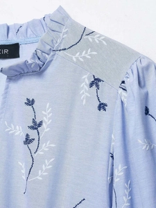 Detail of light blue embroidered dress featuring ruffled collar and floral leaf patterns