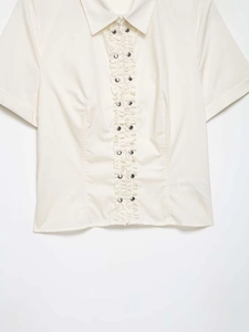 Detail of cream poplin shirt featuring ruffled trim and silver stud accents