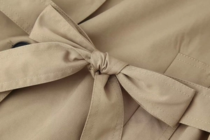Detailed close-up of the adjustable waist tie and khaki fabric texture on the trench coat