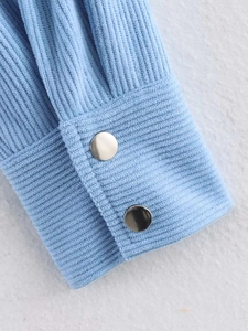 Macro detail of light blue corduroy sleeve cuff with two silver metal snap buttons
