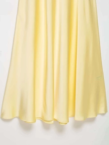 Gros plan sur l'ourlet de la robe midi en satin jaune clair aux plis élégants