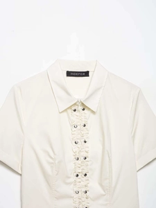 Detail of ruffle trim and silver metal snap buttons on off-white poplin short sleeve shirt