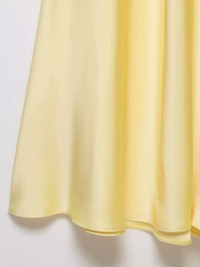 Gros plan sur l'ourlet de la robe midi en satin jaune clair avec texture lisse et plis